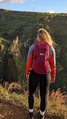 a woman with a red backpack is looking at the mountains and cliffs in the distance