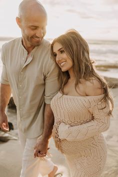 a man and woman walking on the beach holding each other's hand while smiling