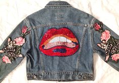 a denim jacket with embroidered lips and roses on the back, sitting on a white sheet