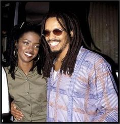 a man with dreadlocks standing next to a woman wearing sunglasses and smiling at the camera