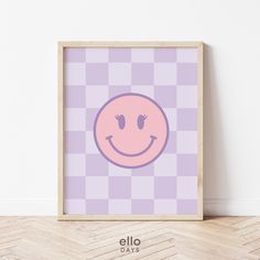 a pink smiley face on a purple checkered background in a wooden frame against a white wall