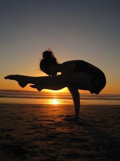 a woman doing yoga on the beach at sunset