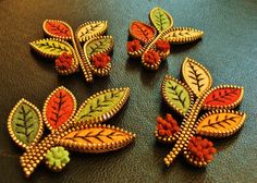 four pieces of colorful broochies sitting on top of a green surface with red, yellow and green leaves