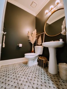 a white toilet sitting next to a sink in a bathroom under a large round mirror