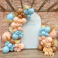 a baby shower balloon arch with balloons and a teddy bear sitting in front of it