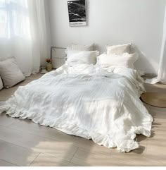 an unmade bed with white linens and pillows on the floor next to a window