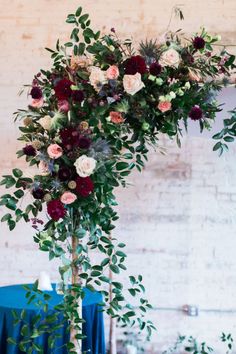 an arrangement of flowers and greenery is displayed on a tall pole in front of a brick wall