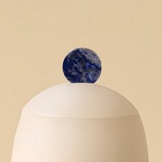 a round object is sitting on top of a white vase with a blue marble ball at the top