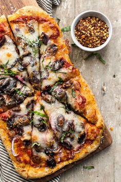 a pizza on a wooden cutting board next to a bowl of seasoning