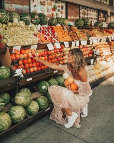 a woman sitting on the ground in front of a fruit stand with watermelon, oranges and melons