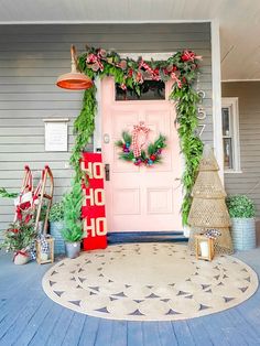 a pink front door decorated for christmas with wreaths and other holiday decorations on the porch