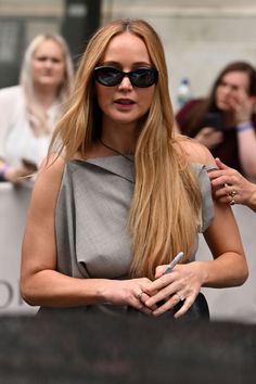 a woman with long hair wearing sunglasses and holding her hand on her hip while standing in front of a crowd