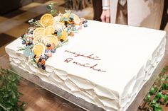 a large white cake with oranges and blueberries on it sitting on a table