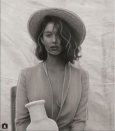 a black and white photo of a woman in a hat with a vase behind her