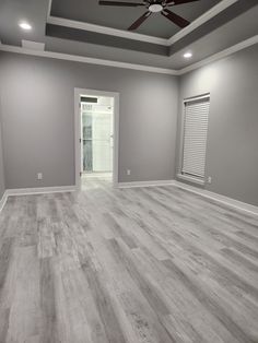 an empty living room with wood floors and ceiling fan in the center, gray walls