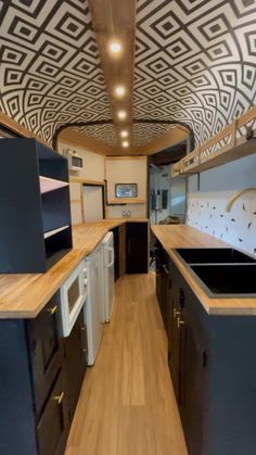 the interior of an rv with wood flooring and black cabinets, white appliances and patterned ceiling