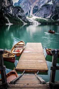 several small boats are docked in the water at a pier on a mountain lake surrounded by snow capped mountains