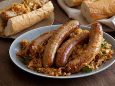 some sausages are on top of rice in a white bowl next to bread rolls