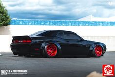 a black sports car with red rims parked in front of an ocean and sky background