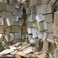 a pile of books sitting next to a lamp on top of a wooden table in front of a wall