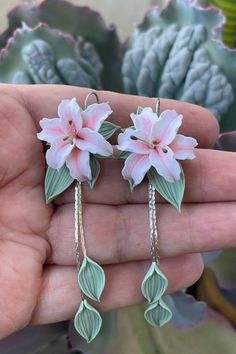 two pink flowers are hanging from the side of a pair of earrings in front of a succulent plant