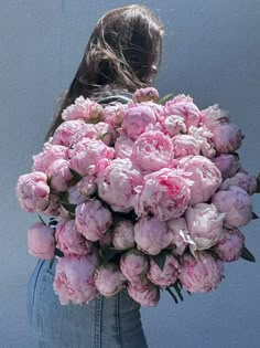 a woman holding a bouquet of pink peonies in her back pocket with water droplets on the petals