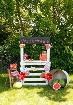 a watermelon stand is set up in the grass with flowers and fruit around it