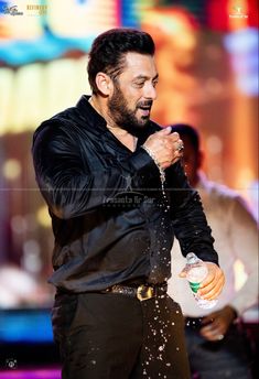 a man in black shirt pouring water on his face and chest with one hand while standing next to him