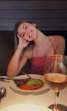 a woman sitting at a table with a plate of food and a glass of wine