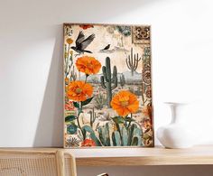 an art piece with orange flowers and cactus plants on the wall next to a white vase