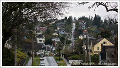 a street with houses on the hill in the back ground and cars driving down it