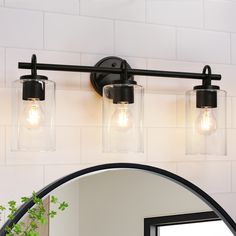 a bathroom vanity light with two clear glass jars on the top and an oval mirror above it