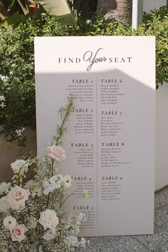 a table plan with white flowers and greenery on the ground next to some bushes