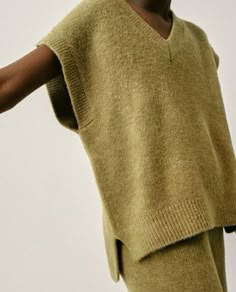 a woman is holding her arm out in front of the camera while wearing a sweater and pants