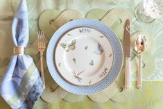 a place setting with blue and white plates, silverware and napkins on a green floral tablecloth