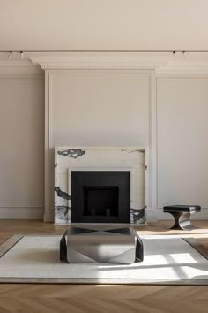 a living room with white walls and a fireplace in the center, surrounded by wood flooring