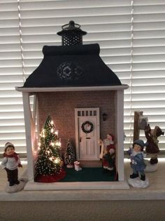 a doll house with christmas decorations and lights on the windowsill, in front of a white shuttered window