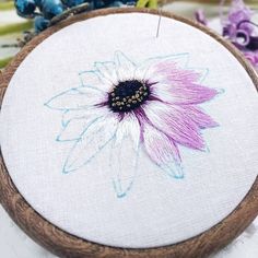 a close up of a embroidery on a wooden hoop with purple and white flowers in the center