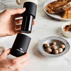 a person is holding a coffee mug over some food on a table with bread and cinnamons