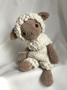 a small stuffed sheep is sitting on a white sheet and wearing a knitted outfit