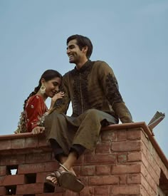 a man and woman sitting on top of a brick wall with their arms around each other