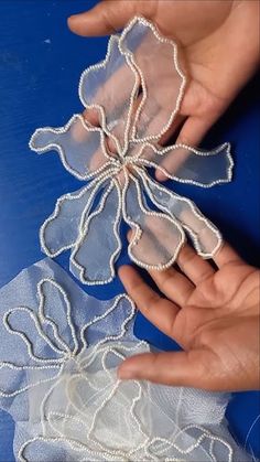 two hands are holding some white lace on a blue tablecloth and another hand is reaching for it