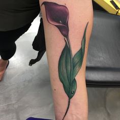 a woman with a tattoo on her arm has a purple flower and green leaves in it