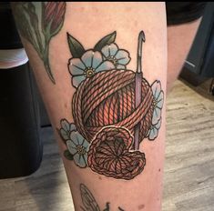 a tattoo on the leg of a woman with yarn and flowers