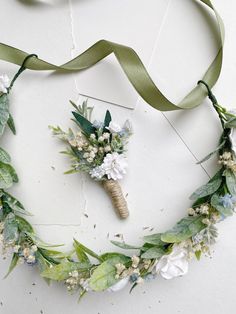 a wreath made out of flowers and greenery on a white surface with a green ribbon