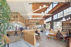 people are sitting at tables and eating in an open space with large windows on the ceiling