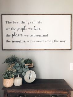 a wooden table topped with plants next to a wall mounted sign that says the best things in life are the people we love