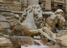 two statues of horses in front of an old building with water running down the side