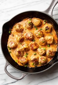 a skillet filled with meatballs and sauce on top of a marble countertop