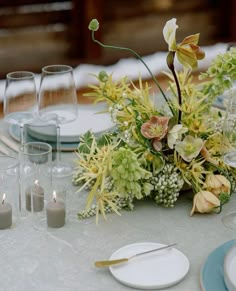 the table is set with plates, silverware and flower centerpieces on it